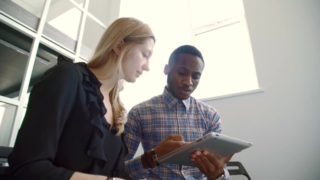 Woman and afroamerican man talking, using tablet in modern office