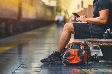 Digital nomad with backpack. Backpacker using a smart phone and a laptop at the train station - obrazy, fototapety, plakaty