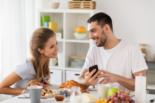 couple with smartphones having breakfast at home