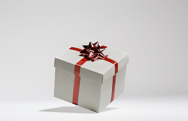 White cube gift box with red stripes and bow floating in grey background