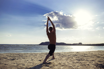 man practices yoga and meditates in the sport position on the beach