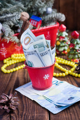 Twisted bills of dollars and euros in red christmas bucket, euro and pink macaroons. New year`s gifts