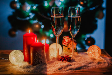Two glasses of champagne on the background of a Christmas tree with candles in darkness with snow