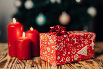 Obraz premium Christmas gift wrapped in gift paper on wooden table on christmas tree bachground with candles 