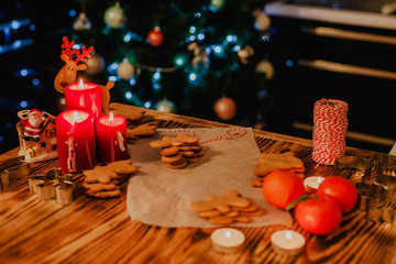 Traditional christmas ginger cookies on woofen background with cutters, candles and red rope. 
