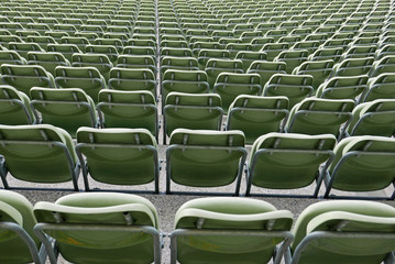 Sitzreihen grüner Plastikstühle in einem Stadion, von hinten gesehen