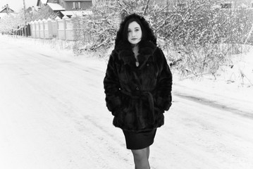 Fototapeta na wymiar Plus size nice young lady in retro look style walk at winter time wear in not natural fur coat. Woman have a good mood. Winter holiday time, black and white photo