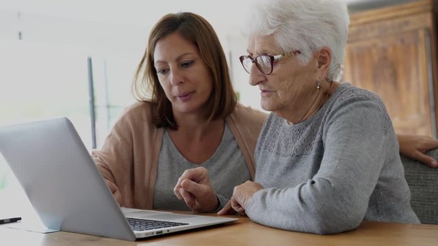 Elderly woman using laptop with help of homecarer