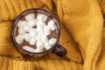 Cozy winter home background, cup of hot coffee with marshmallow on warm orange knitted sweater plaid. Lifestyle concept