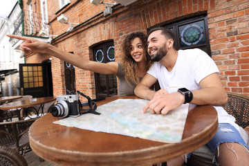 Fototapeta na wymiar Young tourists drinking coffee at cafe and reading city map