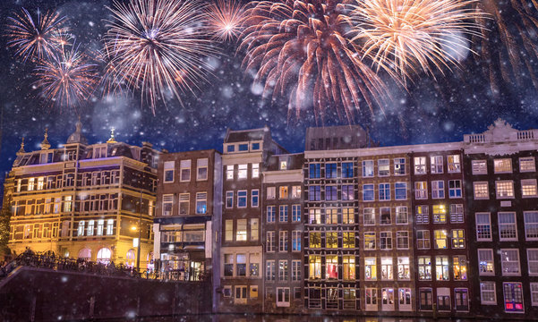 Traditional old buildings and boats at night with fireworks on the black sky in Amsterdam, Netherlands
