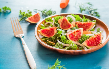 Autumn salad of arugula, figs in a brown earthenware plate on a blue background. top view