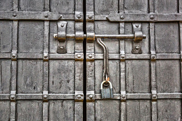 A large metal lock hangs on a fence made of wrought iron
