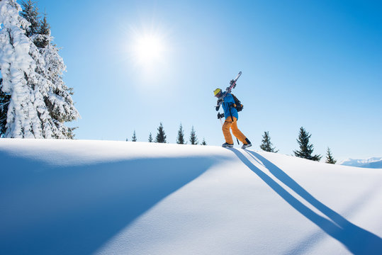 Low angle shot of a skier walking on top of the mountain with his skis on his shoulder on a sunny winter day sunlight nature recreation skiing lifestyle downhill sportive concept