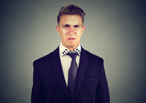 Portrait of a disgusted young business man isolated on gray wall background 