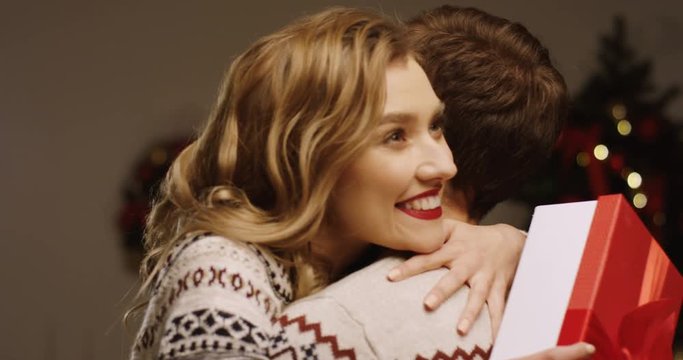 Young happy beautiful woman holding her Christmas present and hugging her boyfriend in the Christmas interior. Young couple in love. Indoor. Portrait shot. Close up