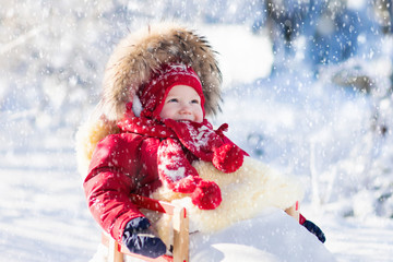 Fototapeta na wymiar Sled and snow fun for kids. Baby sledding in winter park.