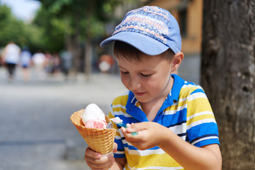 Cute European boy enjoying ice cream cone in a town street.