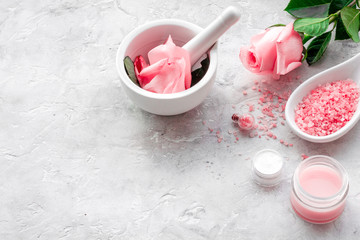 Make cosmetics with rose  oil. Mortar with rose petals and pestle on grey background copyspace