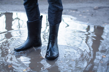Legs of a man in rubber boots walking on deep puddle