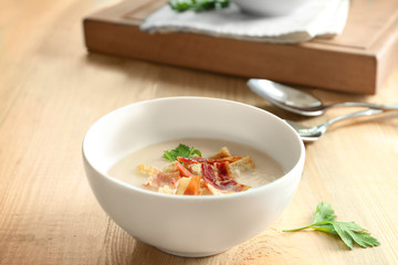 Bowl of yummy potato soup with bacon on wooden table