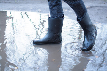 Legs of a man in rubber boots walking on deep puddle