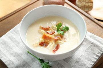 Bowl of yummy potato soup with bacon on wooden table