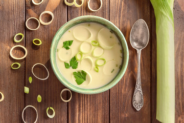 Bowl of yummy potato soup with leek on wooden table