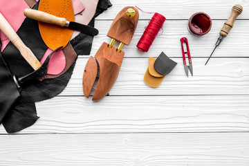 Shoemakers' craft. Tools, wooden last, pieces of leather on white wooden background top view copyspace