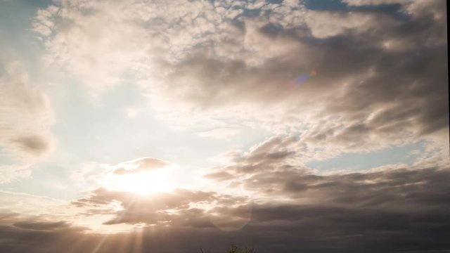 A tilt up timelapse of a cloudy sky at sunset with clouds forming and shaping with sun streaks and flare. 