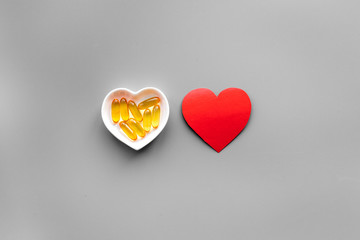 Treat heart. Pills in bowl in shape of heart on grey background top view copyspace