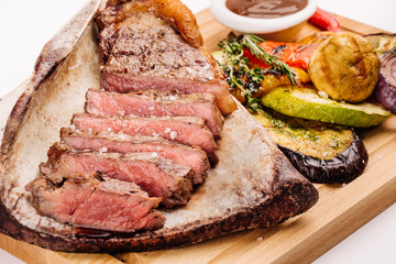 grilled beef steak on the bone with seasonings, fresh rosemary and grilled vegetables on a white background