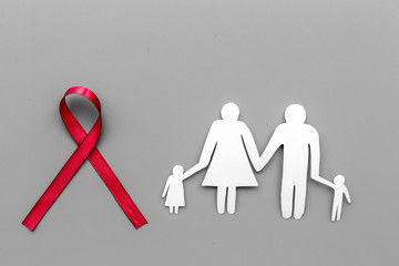 Red ribbon for HIV, AIDS, substance-abuse and anorexia awareness near paper silhouette of family on grey background top view copyspace