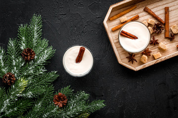 Fototapeta na wymiar Homemade classic eggnog with cinamon and badian on wooden tray near spruce branch, pinecones on black background top view
