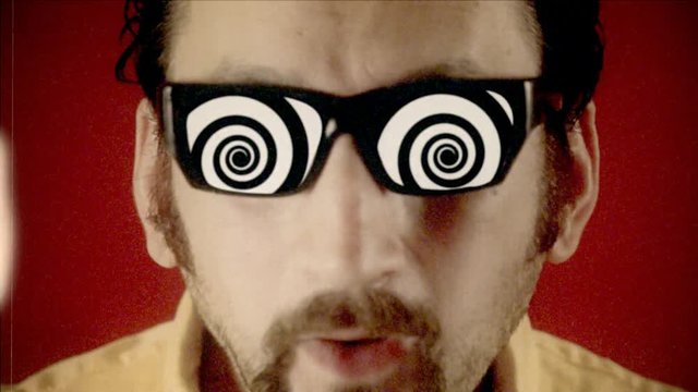 Fake 8mm amateur film: a funny ugly man with hypnotic glasses, looking at a black-and-white animated spiral.
