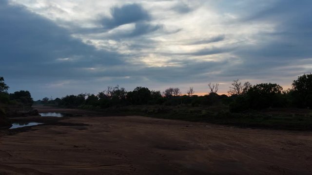 A static early morning sunrise over the Limpopo River bordering South Africa and Botswana with a few puddles of water and scattered clouds. 