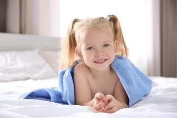 Cute little girl with towel on bed at home