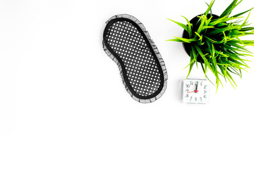 Healthy sleep concept. Sleep mask, plant, alarm clock on white background top view copyspace