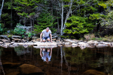 Young man looking into reflection of dark water on peaceful, calm Red Creek river in Dolly Sods, West Virginia