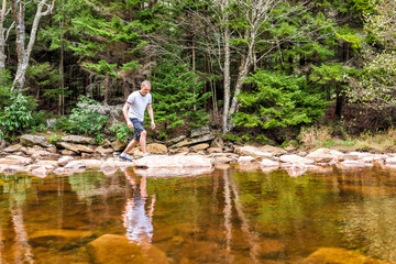 Fototapeta na wymiar Young man crossing peaceful, calm Red Creek river in Dolly Sods, West Virginia during sunny day with reflection