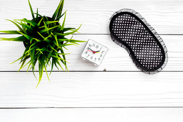 Healthy sleep concept. Sleep mask, plant, alarm clock on white wooden background top view copyspace