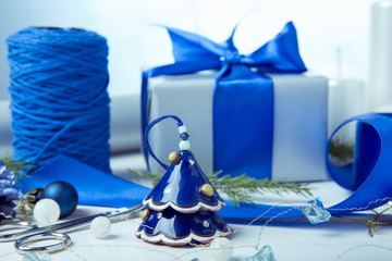 Christmas composition. Packed gift with blue ribbon, pine cones, spruce branches, handmade candles, xmas blue decor on a wooden white background. Gift wrapping process
