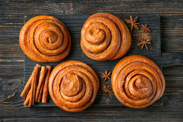 Wooden board with sweet cinnamon rolls on table