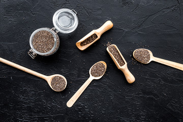 Fototapeta na wymiar Superfood chia seeds in a wooden spoon and scoop on black background top view copyspace