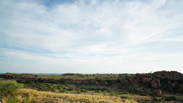 A slow tilt up timelapse of a rocky bushveld landscape with Baobab trees in Botswana/ Mashatu Game Reserve as the clouds pass by and night falls into a starry sky. 