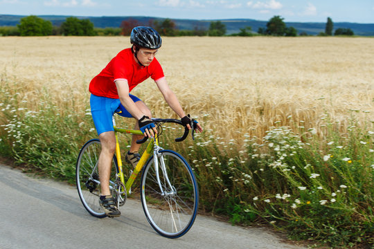 A cyclist rides on a road bicycle along field.