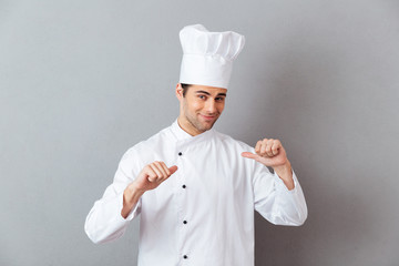 Handsome young cook in uniform pointing to himself.