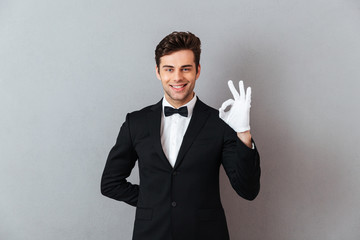 Smiling young waiter showing okay gesture.