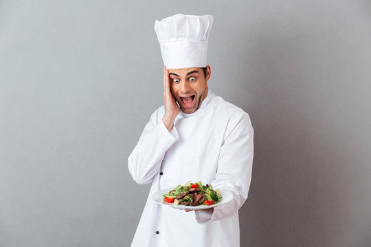 Surprised screaming young cook in uniform holding salad.