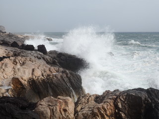 Eine schroffe Küste auf die eine große Welle trifft.